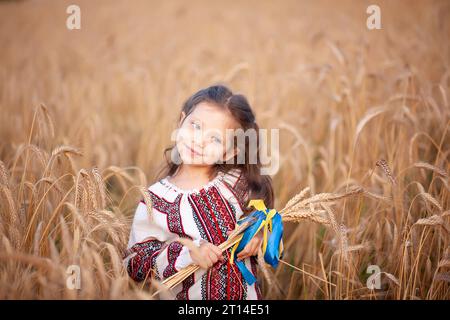 Un bouquet di spikelet di grano legato con un nastro giallo e blu nelle mani di una ragazza in una camicia ricamata. Le mani da vicino si concentrano sulle orecchie di mais. Foto Stock