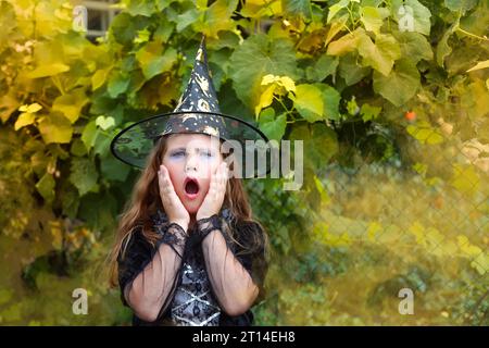 Halloween. piccola strega allegra con una bacchetta magica e il libro evocano e ridono. Foto Stock