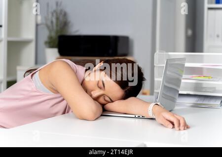 Giovane donna d'affari asiatica adulta che dorme sulla sua scrivania con un pc in ufficio sullo sfondo. - Un concetto di donna d'affari, noioso, esausto, assonnato Foto Stock