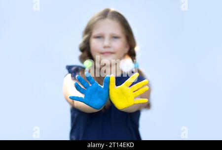 Ragazza felice che mostra i palmi delle mani dipinti in giallo e blu. Indipendenza, bandiera. Giorno della costituzione dell'Ucraina. Educazione, scuola, arte e concetto di pittura Foto Stock