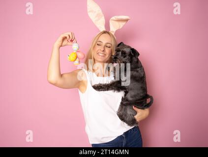 Foto di una bella ragazza bionda che tiene le uova con il suo cane indossa orecchie maglione giallo isolato su sfondo rosa Foto Stock