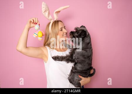 Foto di una bella ragazza bionda che tiene le uova con il suo cane indossa orecchie maglione giallo isolato su sfondo rosa Foto Stock