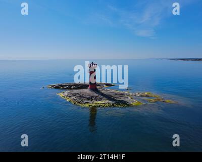 Una vista aerea di un maestoso faro in cima a una piccola roccia nel mezzo di un mare tranquillo Foto Stock
