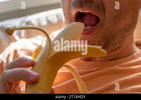 l'uomo tiene una banana sbucciata prima di mangiarla con la bocca aperta Foto Stock