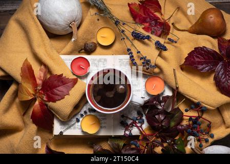 Tema autunnale con frutti e colori autunnali. Un maglione giallo con sopra una tazza di caffè, un libro, foglie autunnali, piccole candele profumate e vari frui Foto Stock