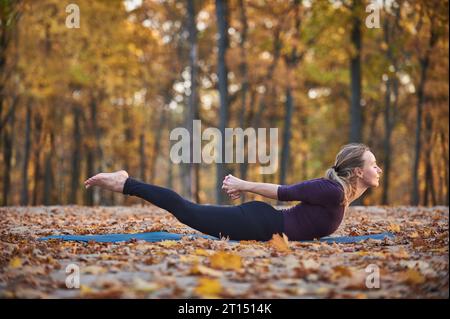 La bella giovane donna pratica yoga asana Salabhasana locust posa sul ponte di legno nel parco autunnale. Foto Stock