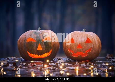 Due zucche sorridenti di Halloween su un tavolo di legno con luci in Una foresta mistica di notte. Foto Stock