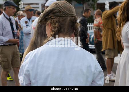 Meccanico femminile con capelli lunghi a coda di cavallo che indossa un berretto in tweed e tute bianche al BARC Revival Meeting 2023, circuito automobilistico di Goodwood, Regno Unito Foto Stock