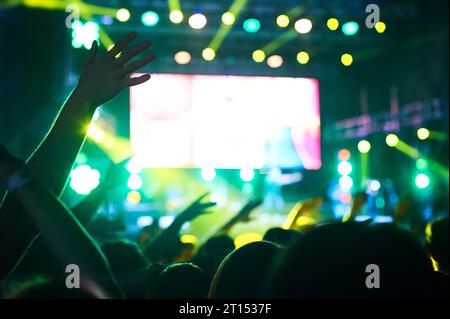 Folla di pubblico con le mani alzate a un festival musicale. Luci che si abbassano dall'alto del palco. Persone irriconoscibili. Foto Stock