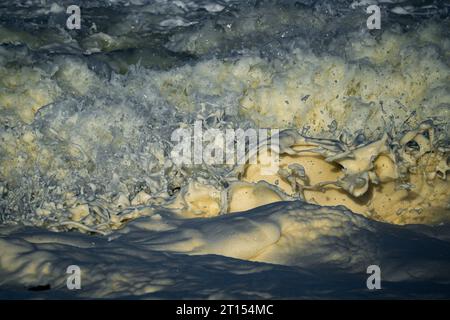Primo piano della foto di schizzi di bolle di schiuma che si schizzano mentre le onde si infrangono sulle rocce Foto Stock