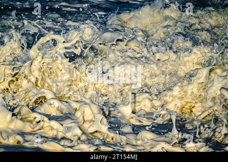 Primo piano della foto di schizzi di bolle di schiuma che si schizzano mentre le onde si infrangono sulle rocce Foto Stock