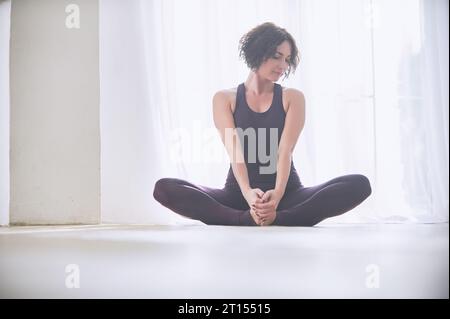 Bella giovane donna le pratiche yoga asana Baddha Konasana - angolo legato pongono in luce studio yoga. Foto Stock