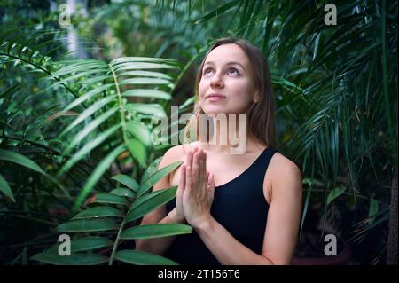 Ritratto di una giovane donna carina che medita e fa la mano nella giungla. Giornata di sole. Foto Stock