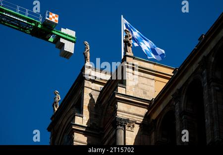 Monaco, Germania. 11 ottobre 2023. Una bandiera bavarese nei colori nazionali del bianco e del blu vola in cima al Maximilianeum, sede del Parlamento bavarese. Una gru da costruzione è in primo piano. Crediti: Sven Hoppe/dpa/Alamy Live News Foto Stock