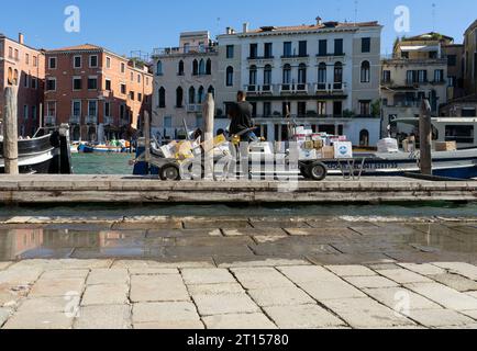 Piccola barca chiamata TOPA per il trasporto di merci nei canali aridi di Venezia, marinai che scaricano merci a casa Foto Stock