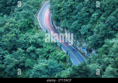 Strada curva attraverso la foresta al tramonto. Vista aerea. Foto Stock
