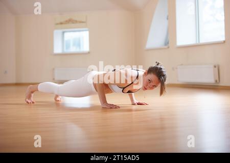 Una bella donna pratica yoga asana chaturanga dandasana - quattro membri del personale si pongono nello studio yoga. Foto Stock