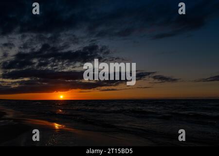 Tramonto arancione sul mare. Onde che si infrangono sulla spiaggia, un cielo spettacolare. Un colpo statico scattato in prima serata Foto Stock
