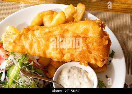 Un tradizionale pasto inglese a base di pesce e patatine fritte servito su un tavolo in un ristorante Fish and Chip. I piatti contengono merluzzo appena pastella e patatine fritte Foto Stock