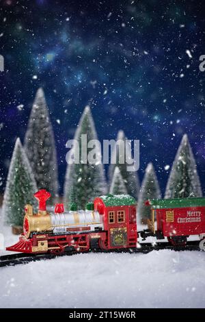 Trenino giocattolo sulla ferrovia nella neve con l'albero di Natale. Sfondo natalizio e Capodanno. Creativa composizione natalizia invernale. Foto Stock