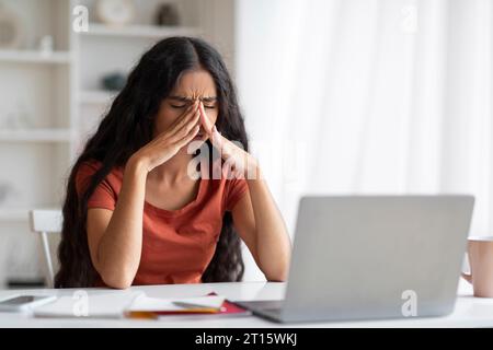 Esausto giovane impiegata di una bruna orientale che lavora su un computer portatile Foto Stock