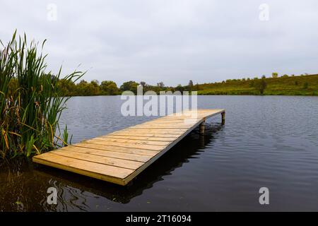 piattaforma di legno sulla riva di uno stagno del villaggio. piattaforma vuota sulla riva di uno stagno in autunno Foto Stock
