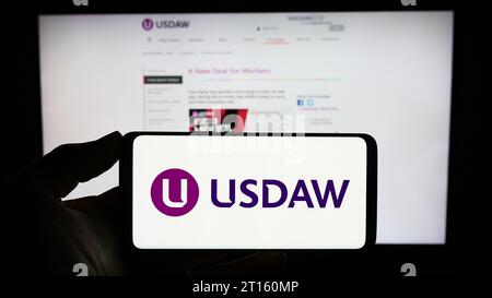 Persona in possesso di un cellulare con il logo di Union of Shop Distributtive and Allied Workers (USDAW) davanti alla pagina Web aziendale. Concentrarsi sul display del telefono. Foto Stock