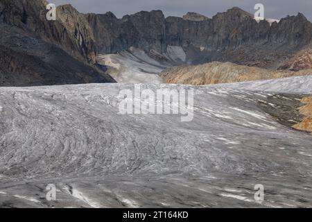 Clima | albedo | Rodano: Due persone possono essere viste al centro di ciò che è rimasto del ghiacciaio Rhona in Svizzera. Nel 2018, il ghiacciaio del Rodano si sciolse più di 70 centimetri di spessore. Secondo un recente rapporto dell'Accademia svizzera delle scienze, lo stesso ghiacciaio ha perso oltre 2 metri di spessore nei due anni del 2022/2023. Mentre la neve è un brillante riflesso dell'energia del sole, il ghiaccio più scuro assorbe invece l'energia, accelerando lo scioglimento del ghiacciaio. Il colore e l'oscurità del ghiaccio glaciale variano in tutto il mondo, a seconda dell'accumulo di inquinamento, dell'età del Foto Stock