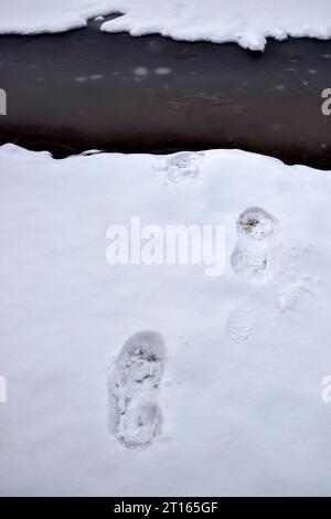 Impronte di scarpe su neve fresca, impronte, orme da uomo. Un ostacolo sotto forma di flusso congelato. Vista dall'alto. Copia spazio. Messa a fuoco selettiva. Foto Stock