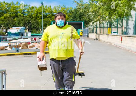 Lavoratore in una fabbrica di riciclaggio o in un punto pulito e spazzatura con una maschera facciale e con protezioni di sicurezza, nuovo normale, pandemia di coronavirus, covid-19. Foto Stock