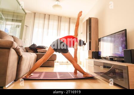 Una giovane donna che fa yoga si allunga nel suo salotto. Nella quarantena del coronavirus Foto Stock