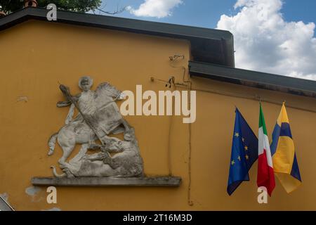 Un bassorilievo raffigurante San Giorgio e il Drago accanto alle bandiere sulla facciata di un edificio, Parma, Emilia-Romagna, Italia Foto Stock