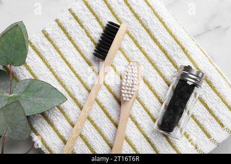 Spazzolini da denti in bambù, filo interdentale naturale, asciugamano e ramo di eucalipto su tavolo in marmo bianco, posizione piatta Foto Stock