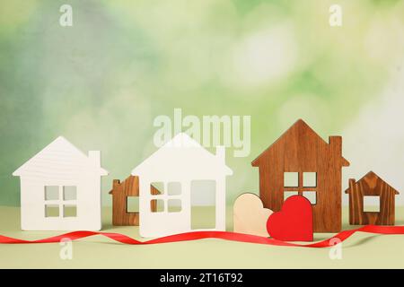 Concetto di relazione a distanza. Modelli di casa, cuori decorativi e nastro rosso su sfondo verde chiaro Foto Stock