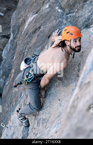 Persona che sale in alta montagna con corda senza camicia e casco arancione nella natura selvaggia. Concetto di fiducia e rischio, sicurezza e auto-miglioramento. Foto Stock