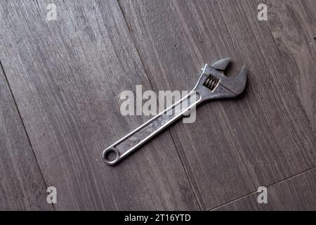 Quando una chiave regolabile, lanciata ad angolo, colpisce il pavimento in legno duro Foto Stock