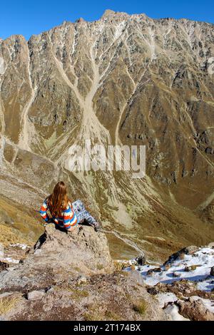 La ragazza seduta sulla scogliera dell'enorme roccia che domina le alte montagne della regione di Elbrus, Caucaso russo Foto Stock