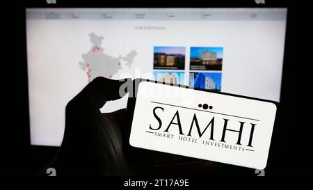 Persona in possesso di un cellulare con il logo della società indiana di sviluppo alberghiero Samhi Hotels Ltd. Davanti alla pagina Web aziendale. Concentrarsi sul display del telefono. Foto Stock