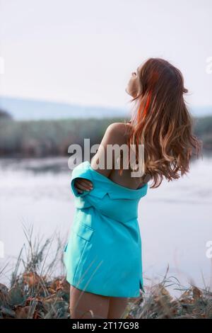 Bella donna che cammina vicino al lago, giacca blu e capelli tinti rossi Foto Stock