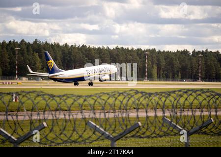 Un aereo decolla dalla pista dell'aeroporto con uno sfondo verde di alberi sul retro e una recinzione in filo spinato in primo piano Foto Stock