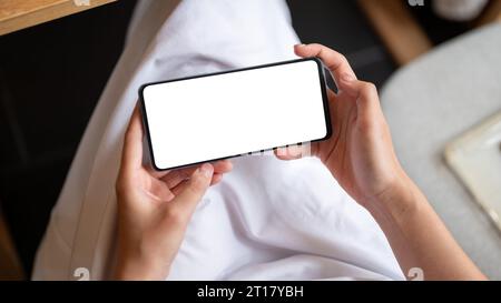 Immagine ravvicinata di un modello di smartphone con schermo bianco in posizione orizzontale nelle mani di una donna. Una donna che usa lo smartphone mentre si rilassa in un bar. Foto Stock