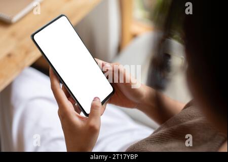 Immagine ravvicinata di una donna che usa lo smartphone mentre si rilassa in un bar. Un modello di smartphone con schermo bianco nelle mani di una donna. Persone e techno Foto Stock