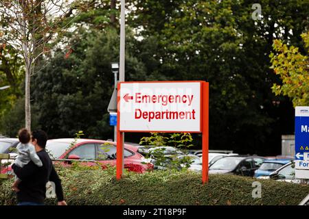 Sfocati uomo e bambino che camminano in direzione del reparto di emergenza dopo il cartello del reparto di emergenza rosso all'ospedale Royal Devon & Exeter Foto Stock