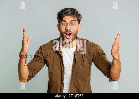 Oh mio Dio, wow. Entusiasta e stupito uomo vincitore che alza le mani di sorpresa guardando la fotocamera con grandi occhi, scioccato dall'improvvisa vittoria che celebra il successo ottenuto buone notizie. Ragazzo su sfondo grigio Foto Stock