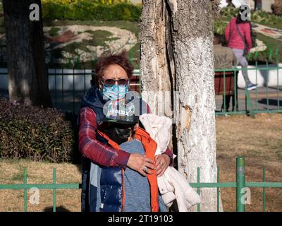 La Paz, Bolivia - 8 agosto 2022: La donna boliviana che indossa occhiali e una maschera di protezione Covid-19 abbraccia suo nipote, che indossa anche un berretto e una M Foto Stock