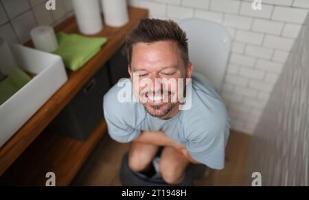 Uomo con sorriso soddisfatto si siede sulla toilette Foto Stock