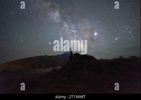 Silhouette di un uomo in piedi su uno sperone roccioso di notte, Thailandia Foto Stock