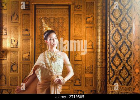 Donna sorridente in abito tradizionale di fronte a un muro decorato, Thailandia Foto Stock