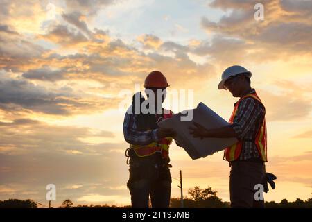 Due operai edili che guardano i piani di un cantiere, Thailandia Foto Stock