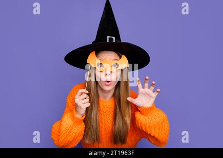 Foto di una giovane ragazza che inganna dietro la maschera di pipistrello mascherata festa di halloween terrificante strega dire boo isolato su sfondo di colore viola Foto Stock